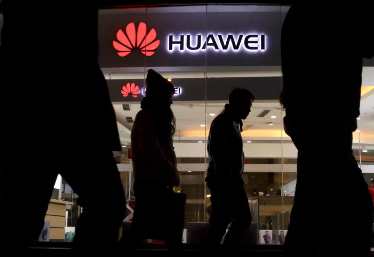 Pedestrians walk past a Huawei retail shop in Beijing Thursday, Dec. 6, 2018. China on Thursday demanded Canada release a Huawei Technologies executive who was arrested in a case that adds to technology tensions with Washington and threatens to complicate trade talks.