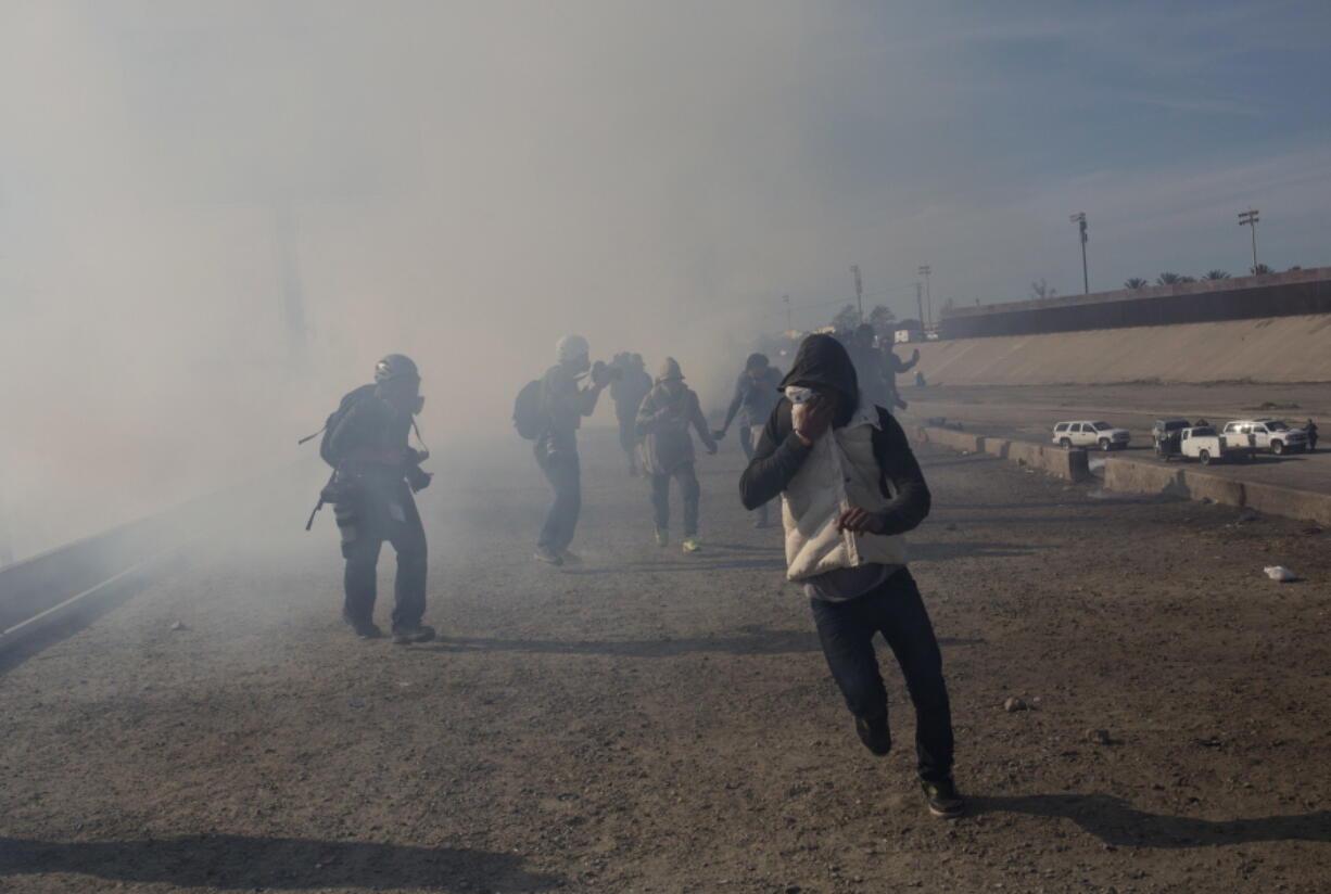 FILE - In this Nov. 25, 2018, file photo, migrants run from tear gas launched by U.S. agents, amid photojournalists covering the Mexico-U.S. border, after a group of migrants got past Mexican police at the Chaparral crossing in Tijuana, Mexico. Children torn from their parents, refugees turned away, tear gas fired on asylum-seekers, and a swath of the globe derided by the president in crude language. In a breathless 2018, they were just a handful of headlines on immigration, one of the year’s most dominant issues.