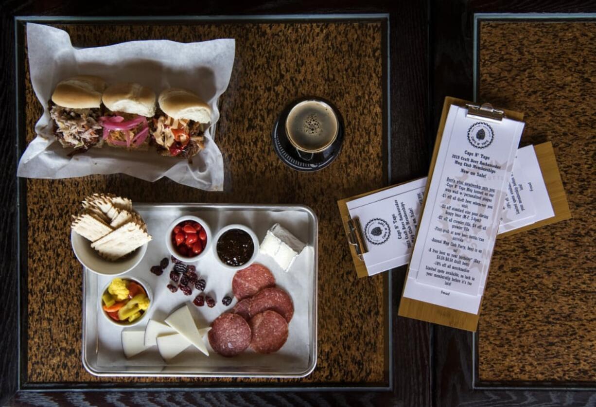 The Wendy and Erica cheese and charcuterie plate, bottom left, the classic, buffalo and Thai pulled pork sliders, top left, and the Silver Moon Dark Side Stout, right, at Caps N’ Taps.