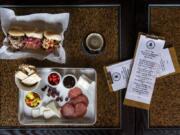 The Wendy and Erica cheese and charcuterie plate, bottom left, the classic, buffalo and Thai pulled pork sliders, top left, and the Silver Moon Dark Side Stout, right, at Caps N’ Taps.