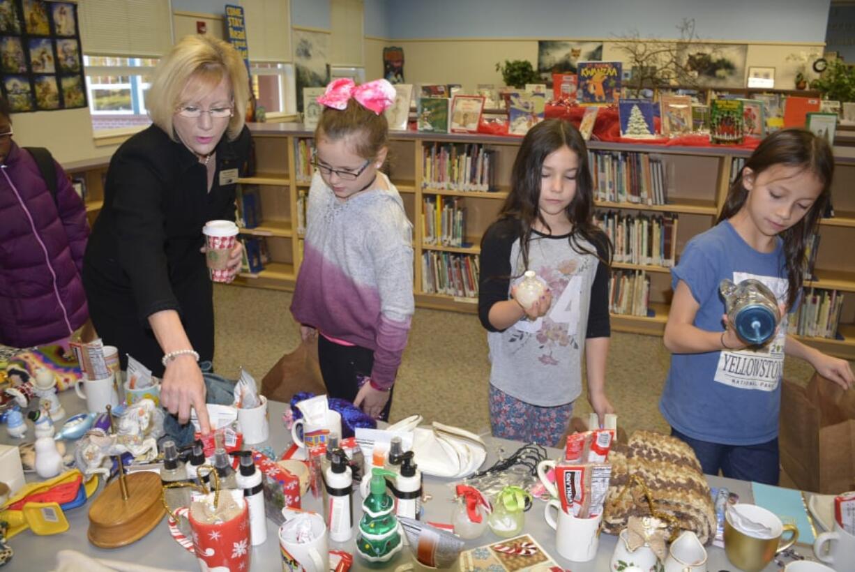 Washougal: Washougal Superintendent Mary Templeton, from left, helps students Madison Reaves, Hannah Hassing and Tessandra Townsend look for presents at Hathaway Elementary School’s gift store.