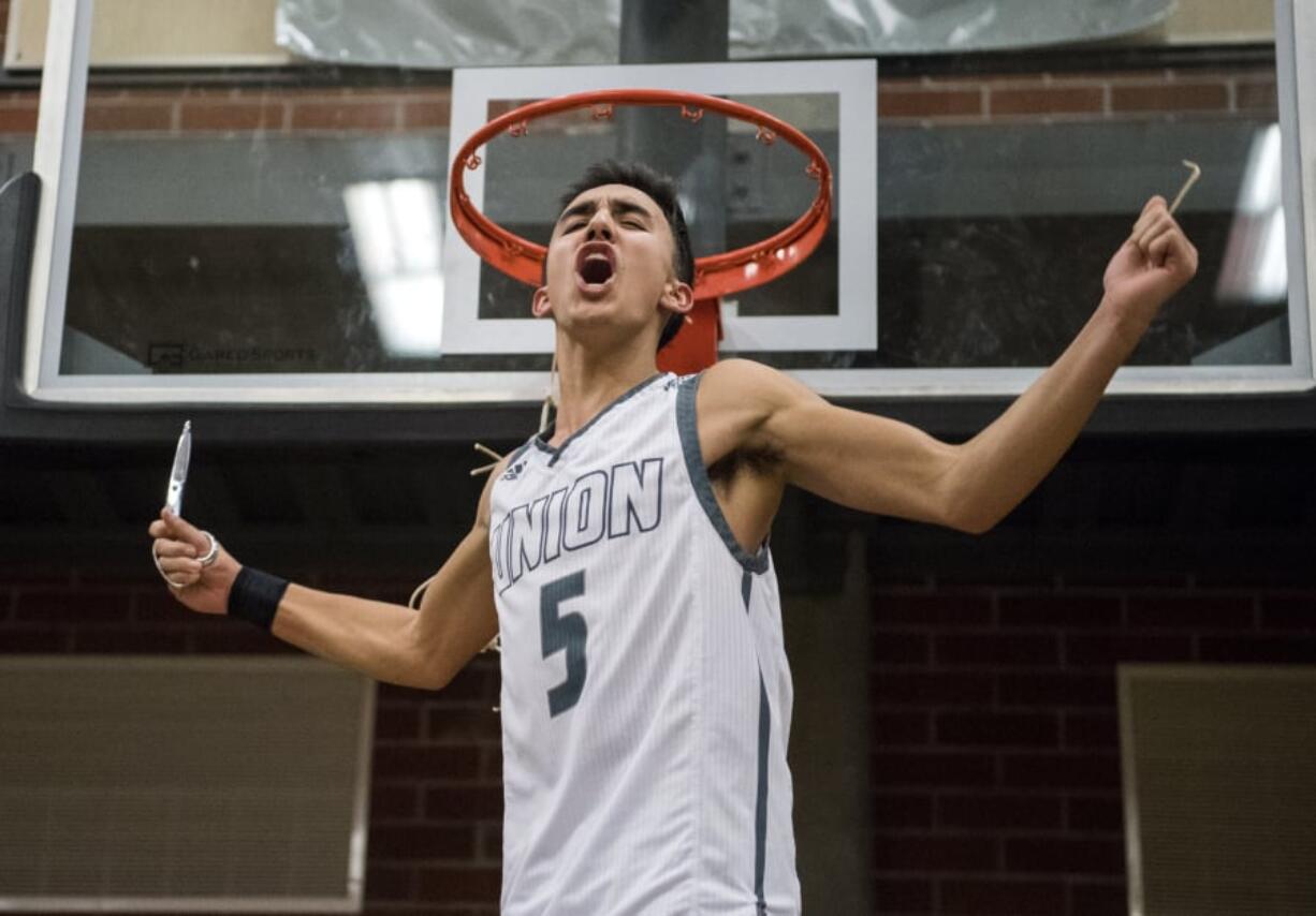 Houston Combs cuts a piece of the basketball net after Union defeated Skyview on Wednesday to win the 4A Greater St. Helens League title.