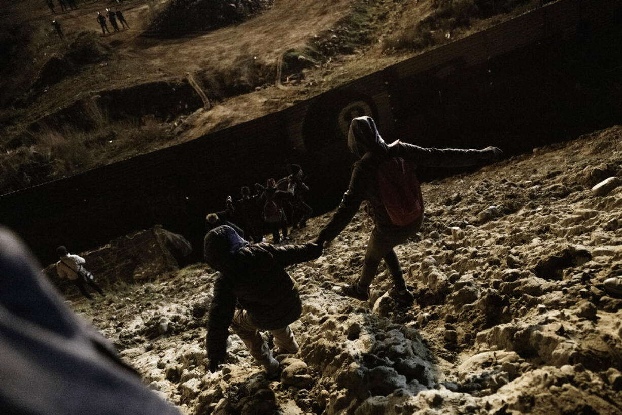 Migrants walk towards the border fence under surveillance of U.S. Border patrols as they attempt to get into the U.S. side to San Diego, Calif., from Tijuana, Mexico, Tuesday, Jan. 1, 2019. Discouraged by the long wait to apply for asylum through official ports of entry, many migrants from recent caravans are choosing to cross the U.S. border wall and hand themselves in to border patrol agents.