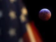 A U.S. Flag in downtown Washington flies in front of the moon during a lunar eclipse, Sunday, Jan. 20, 2019. The entire eclipse will exceed three hours. Totality - when the moon’s completely bathed in Earth’s shadow - will last an hour. Expect the eclipsed, or blood moon, to turn red from sunlight scattering off Earth’s atmosphere. (AP Photo/J.