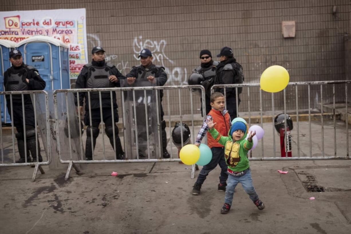 Children play with balloons in front of Federal Police outside an empty warehouse used as a shelter set up for migrants in downtown Tijuana, Mexico, Saturday, Jan. 5, 2019. Authorities ordered the shelter to be closed due to sanitary conditions. Discouraged by the long wait to apply for asylum through official ports of entry, many migrants from recent caravans are choosing to cross the U.S. border wall and hand themselves in to border patrol agents.