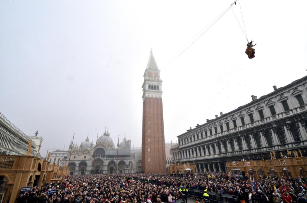 FILE - In this Sunday, Jan. 31, 2016 filer, people fill St. Mark’s Square in Venice, Italy, to watch the ‘ Flight of the Angel ‘, as a woman dressed in traditional costume descends from the bell tower into the square. The mayor of Venice says Italy’s new budget law includes a measure allowing the lagoon city to charge all visitors for accessing the historic center -- not just those sleeping in hotels or other accommodations. Mayor Luigi Brugnaro announced on Twitter late Sunday, Dec. 30, 2018 that the tax will ‘‘allow us to manage the city better and to keep it clean,’’ and ‘‘above all allow Venetians to live with more decorum.’’ The city council will determine the amount of the tax and collection mode.