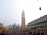 FILE - In this Sunday, Jan. 31, 2016 filer, people fill St. Mark’s Square in Venice, Italy, to watch the ‘ Flight of the Angel ‘, as a woman dressed in traditional costume descends from the bell tower into the square. The mayor of Venice says Italy’s new budget law includes a measure allowing the lagoon city to charge all visitors for accessing the historic center -- not just those sleeping in hotels or other accommodations. Mayor Luigi Brugnaro announced on Twitter late Sunday, Dec. 30, 2018 that the tax will ‘‘allow us to manage the city better and to keep it clean,’’ and ‘‘above all allow Venetians to live with more decorum.’’ The city council will determine the amount of the tax and collection mode.