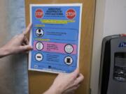 Registered nurse Rebecca Montero holds a sign on the door of the negative pressure airflow room at PeaceHealth Southwest Medical Center in Vancouver.