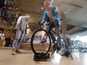 FILE- In this Nov. 13, 2018, photo Vitalii Myroshnychenko, right, test rides a bike atop a stand as Denis Rybalchenko looks on in REI Co-op’s flagship store in Seattle. The usual advice is “buy experiences, not things.” But that requires a deeper dive. A bicycle can provide an experience, and a new camera can preserve one. So buy experiences, especially with other people, but also think about buying material things that allow you to have experiences or enhance them.