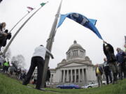 Washington Gov. Jay Inslee, center-left, turns a crank to raise a Seattle Seahawks 12 flag, Thursday at the Capitol in Olympia. The Seahawks will play the Dallas Cowboys Saturday in an NFL football wild-card playoff game. Ted S.