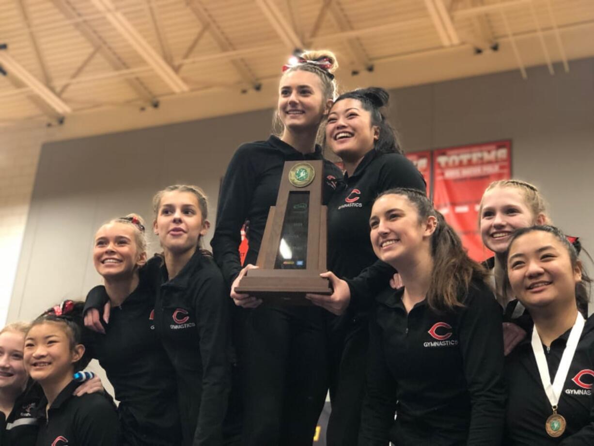 Camas gymnastics team members hoist the state championship trophy on the podium at state.