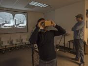 Barrie Buckner, GTMA director of partnerships, center, views an apartment in virtual reality using his smartphone while CEO Joshua Swanson watches. The image on the projector screen shows what Buckner is seeing; each eye views one of the two images, creating what the viewer perceives as a single three-dimensional view.