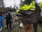 Cpl. Rey Reynolds joins employees of Rapid Response Bio Clean, a company the city contracts with to clean up homeless camps. The Vancouver Police Department previously posted a notice at the camp, telling the occupants they were in violation of the city’s camping ordinance.