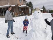 Terrance Crane, left, and Modesty Van Dusen, 5, watch neighbor Alex Cox, 10, add a stick arm to a snowman Sunday in Camas.