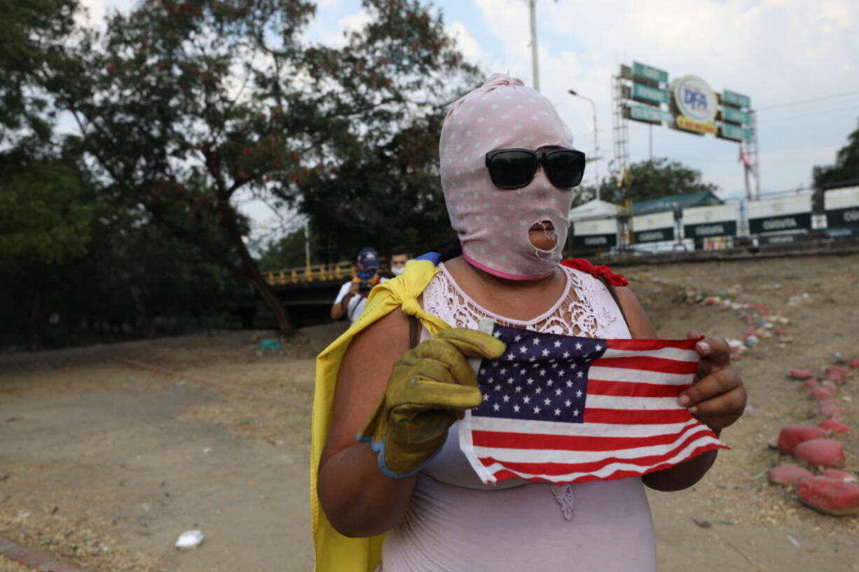 A masked opposition demonstrator holds a United States flag after clashing with members of the Venezuelan Bolivarian National Guard at the Francisco de Paula Santander International Bridge, in Cucuta, Colombia, Tuesday, Feb. 26, 2019. Over the weekend, security forces on the borders with Colombia and Brazil fired tear gas and buckshot on activists waving Venezuelan flags while escorting trucks with emergency medical and food kits. Four people were killed and at least 300 wounded, although only a few were hospitalized.