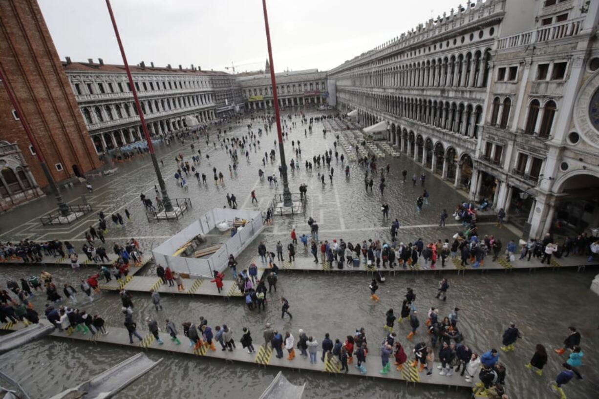 FILE - In this Thursday, Nov. 1, 2018 file photo, tourists walk in flooded St. Mark’s Square in Venice, Italy. Venice’s city council late Tuesday, Feb. 26, 2018, approved a visitors tax on day-trippers, aimed at paying for essential services that are more costly to perform in the lagoon city, such as trash collection and the cleaning of public areas.