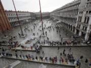 FILE - In this Thursday, Nov. 1, 2018 file photo, tourists walk in flooded St. Mark’s Square in Venice, Italy. Venice’s city council late Tuesday, Feb. 26, 2018, approved a visitors tax on day-trippers, aimed at paying for essential services that are more costly to perform in the lagoon city, such as trash collection and the cleaning of public areas.