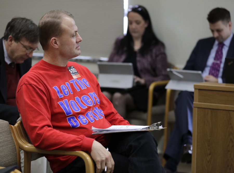 Anti-tax initiative promoter Tim Eyman, center, waits before speaking during a Feb. 13 public hearing of the Senate State Government, Tribal Relations, and Elections Committee at the Capitol in Olympia. Eyman testified Tuesday in favor of his “Bring Back Our $30 Car Tabs” initiative.