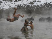 In this Thursday, Jan. 24, 2019 photo, Muhammed Toren, 18, left, and Berkan Toren, 20, enjoy a hot spring along with their water buffaloes near the village of Budakli, in the mountainous Bitlis province of southeastern Turkey. Residents of the village with some 60 homes walk hundreds of buffaloes up snow-covered roads to the geothermal springs in the winter. Villagers say the hot springs heal buffaloes’ wounds, alleviate discomfort in their breasts and make quality milk. The village’s main source of income is cheese, butter and milk from the buffaloes.