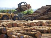 A log loader picks up a load of timber from a truck.