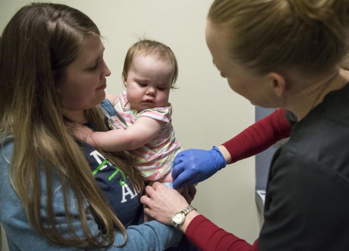 Tamine Robinson holds her 1-year-old daughter Riley, both of Battle Ground, as registered nurse Julie Ward fixes a bandage on Riley’s leg after administering the measles, mumps and rubella vaccine during a free vaccination clinic March 1, 2019, at Legacy Medical Group’s Family Wellness office in Vancouver.