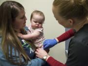 Tamine Robinson holds her 1-year-old daughter Riley, both of Battle Ground, as registered nurse Julie Ward fixes a bandage on Riley’s leg after administering the measles, mumps and rubella vaccine during a free vaccination clinic March 1, 2019, at Legacy Medical Group’s Family Wellness office in Vancouver.