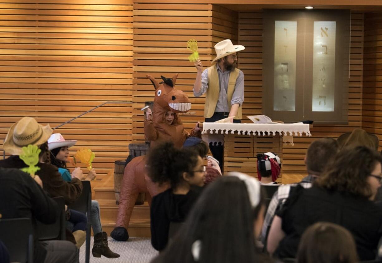 Efraim Greenberg, 10, stands next to his father, Rabbi Shmulik Greenberg, as the rabbi reads in Hebrew from the Megillah, the Book of Esther, to commemorate Purim, a joy-filled Jewish holiday.