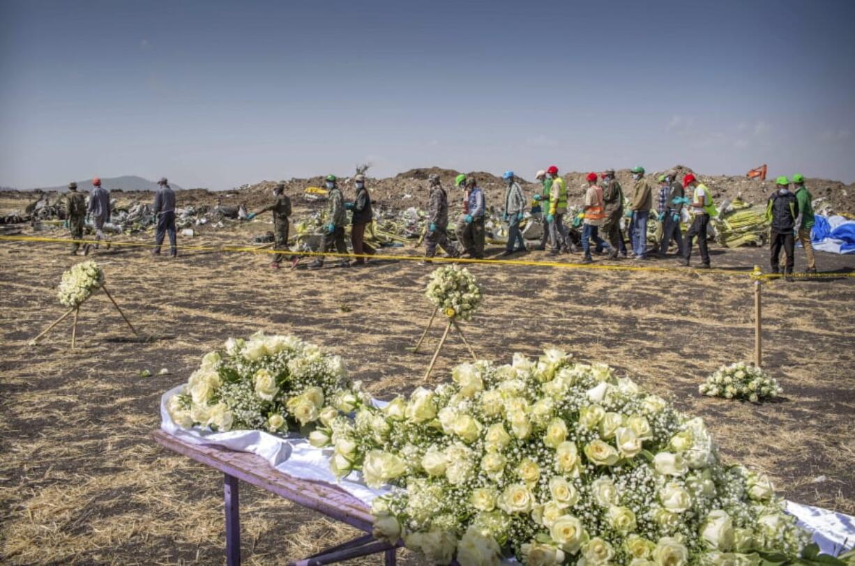 Workers walk past flowers laid at the scene of the Ethiopian Airlines Boeing 737 Max 8 crash Wednesday south of Addis Ababa, Ethiopia.