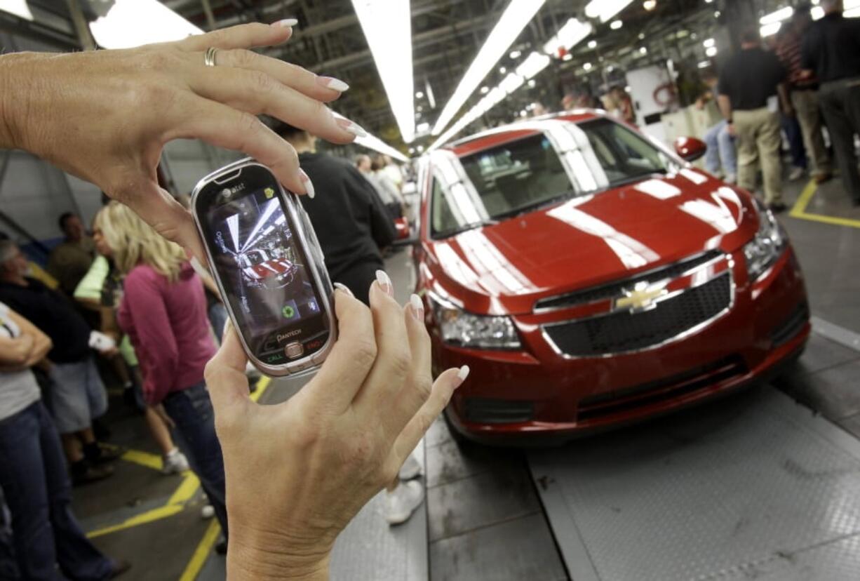 FILE - In this Sept. 8, 2010, file photo, an auto worker takes a picture of the first Chevrolet Cruze compact sedan to come off the assembly line at a ceremony inside the GM factory in Lordstown, Ohio. GM employees in Lordstown and other factories in Michigan and Maryland that are targeted to close within a year say moving will force them to leave behind relatives, even their children, in some cases.