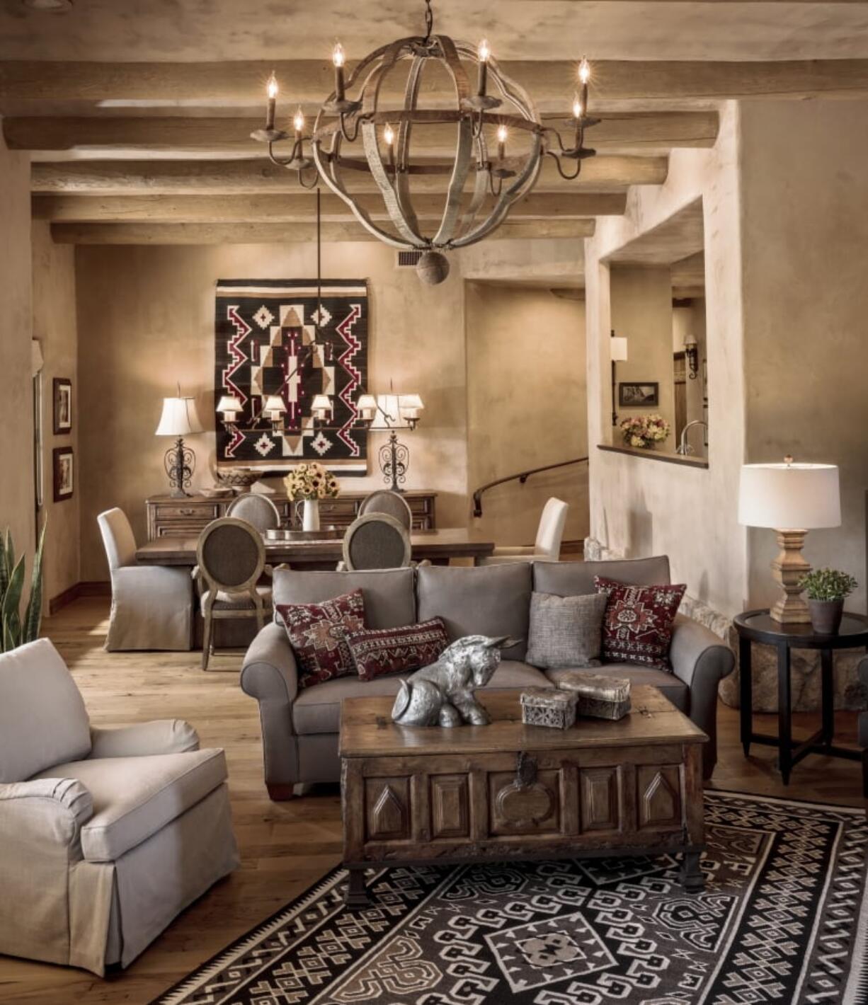 The combination living-dining room in a Santa Fe home in the mountains in Tucson, Ariz. The home was remodeled with chestnut board floors, hand-applied plaster, viga-style beams, and furnishings including a wood trunk from South America, a pair of antique iron lamps made from a reclaimed balcony rail from Spain, two antique Navajo rugs and a collection of old pueblo pottery and antique Apache baskets.