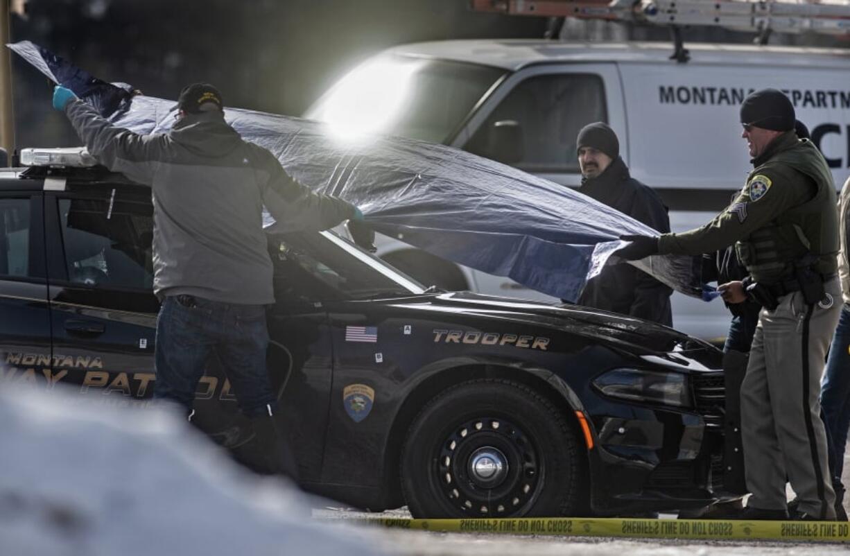 Law enforcement cover Montana State Trooper Wade Palmer’s car at the scene of the shooting near the Evaro Bar on Friday, March 15, 2019, in Missoula, Mont. Palmer, who was investigating an earlier shooting, was himself shot and critically injured early Friday after finding the suspect’s vehicle, leading authorities to launch an overnight manhunt that ended in the arrest of a 29-year-old man, officials said.