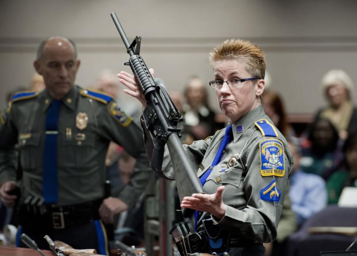 FILE - In this Jan. 28, 2013, file photo, firearms training unit Detective Barbara J. Mattson, of the Connecticut State Police, holds a Bushmaster AR-15 rifle, the same make and model used by Adam Lanza in the 2012 Sandy Hook School shooting, during a hearing at the Legislative Office Building in Hartford, Conn. A divided Connecticut Supreme Court ruled, Thursday, March 14, 2019, gun maker Remington can be sued over how it marketed the Bushmaster rifle used in the massacre.