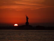 FILE - In this July 1, 2018 file photo, the sun sets behind the Statue of Liberty in New York as record high temperatures were recorded over the week in the U.S. and elsewhere. An AP data analysis of records from 1999-2019 shows that in weather stations across America, hot records are being set twice as often as cold ones.