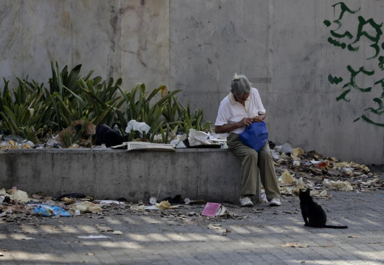 A woman sits on a concrete planter surrounded by litter, in Caracas, Venezuela, Tuesday, March 26, 2019.