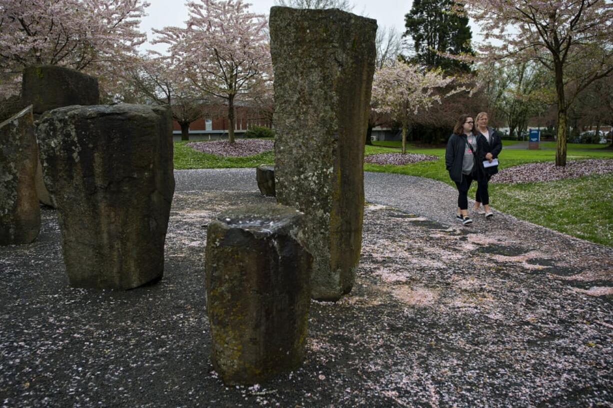 Delaney Lewis, 19, of Battle Ground, left, keeps in step with her mom, Krystopher, as they stroll through a blanket of blossoms knocked off trees by spring rains at Clark College on Monday afternoon while touring the school.