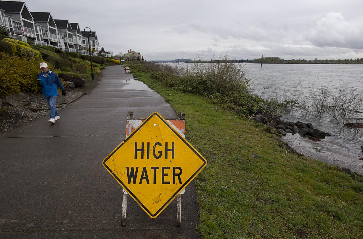 Water from the Columbia River begins to creep up onto the pathway near Columbia Shores Condominium as Vancouver resident Richard Allen strolls past Thursday morning, April 11, 2019.