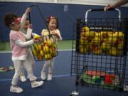 Fiona Chang, from left, and her triplet sisters, Madeline and Amelia, all 4 and of Camas, help clean up balls during a tennis lesson at Vancouver Tennis Center. Wendy Chang, the triplets’ mom, won a state championship at Bellevue High School, and was on Yale University’s tennis team.