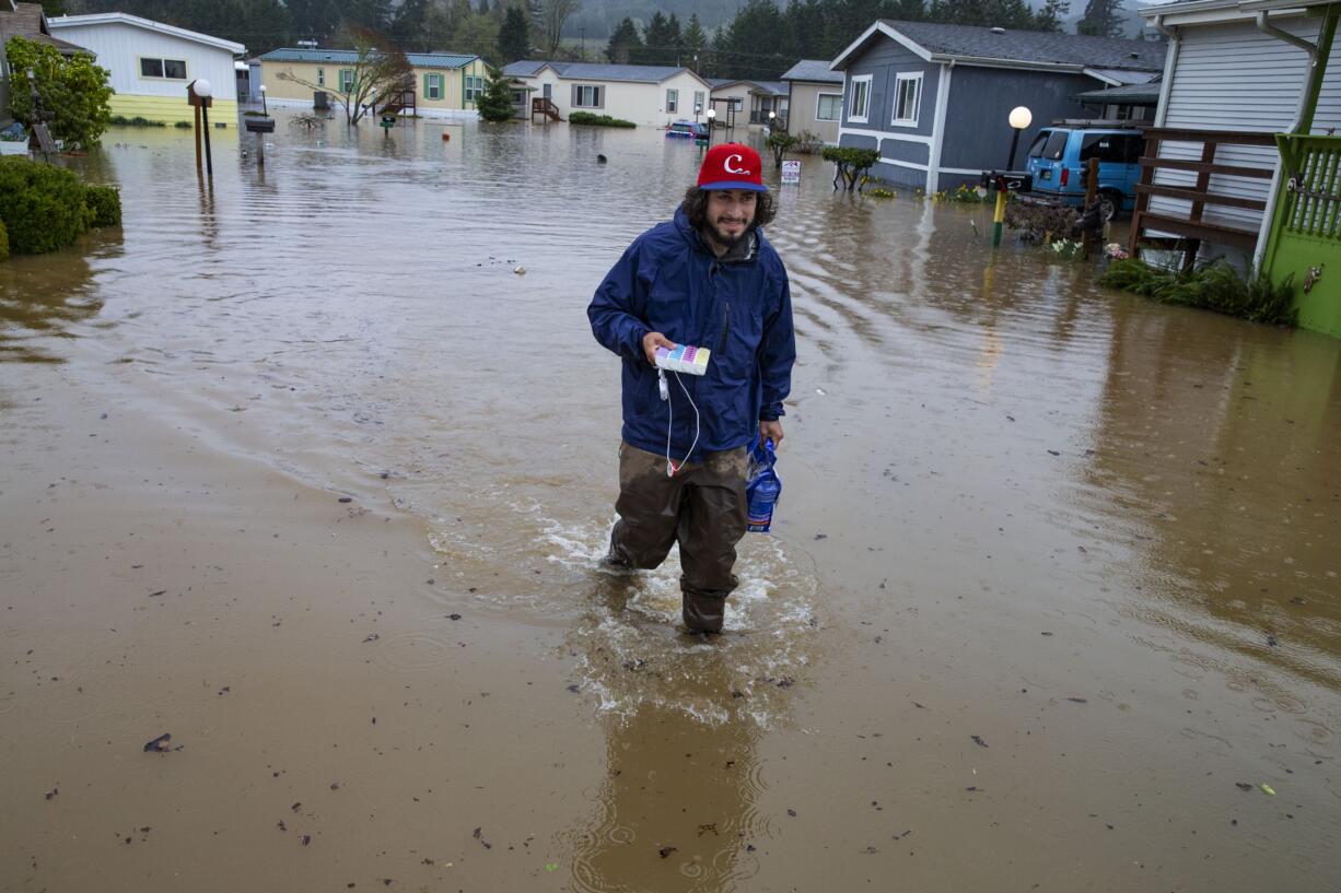 Jett Archuleta wades through a flooded street in the Riverstone Mobile Home Park in Cottage Grove to retrieve medications for his Grandfather Merle Wright and dog treats for Wright's dog Betty Monday, April, 8, 2019 after flood waters rose overnight.