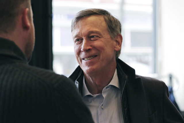 In this March 22, 2019, file photo, former Democratic Colorado Gov. John Hickenlooper talks with AmeriCorps members prior to a roundtable campaign stop in Manchester, N.H. Hickenlooper is proposing a $15 federal minimum wage [--] with a twist. Rather than unilaterally hiking the national wage to $15, the former Colorado governor proposes phasing in the increases based on the cost of living.