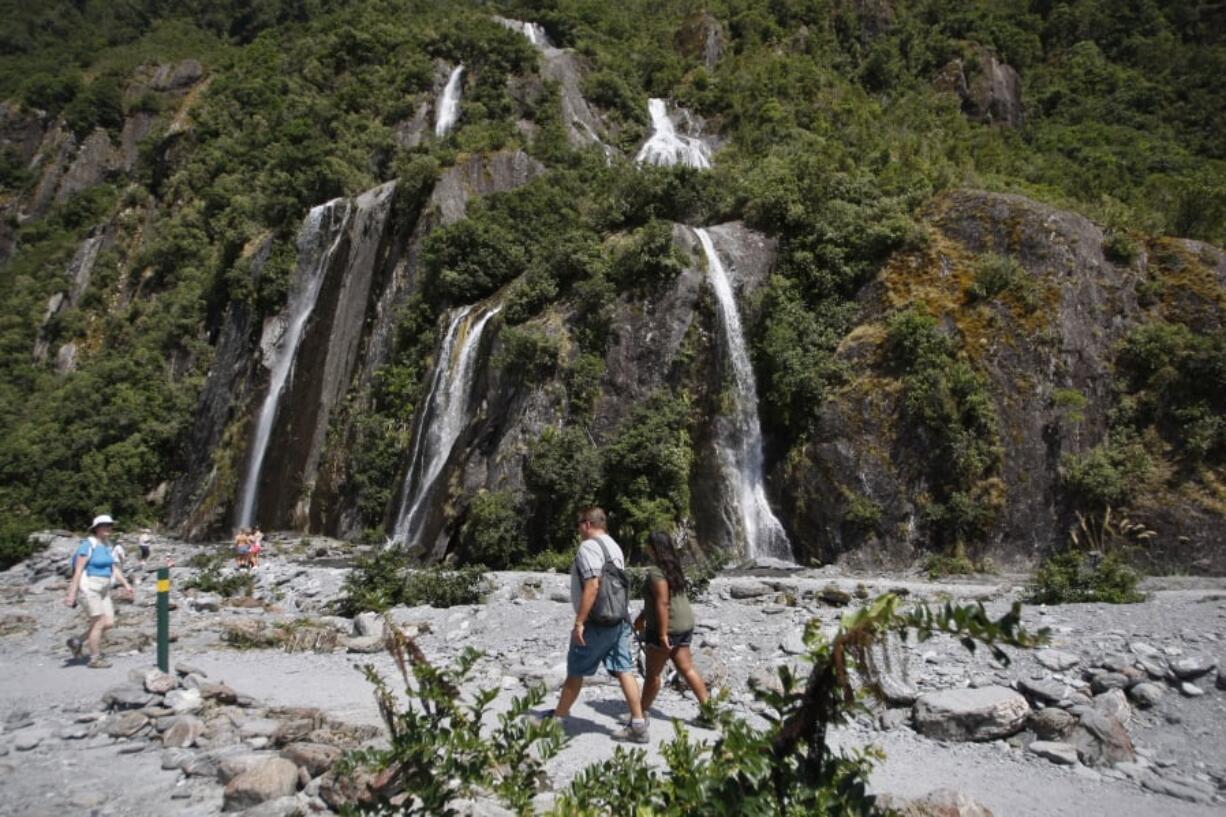 In this Feb. 7, 2016 file photo, tourists walk past waterfalls at the Franz Josef Glacier in New Zealand. The Fox and Franz Josef glaciers have been melting at such a rapid rate that it has become too dangerous for tourists to hike onto them from the valley floor, ending a tradition that dates back a century.