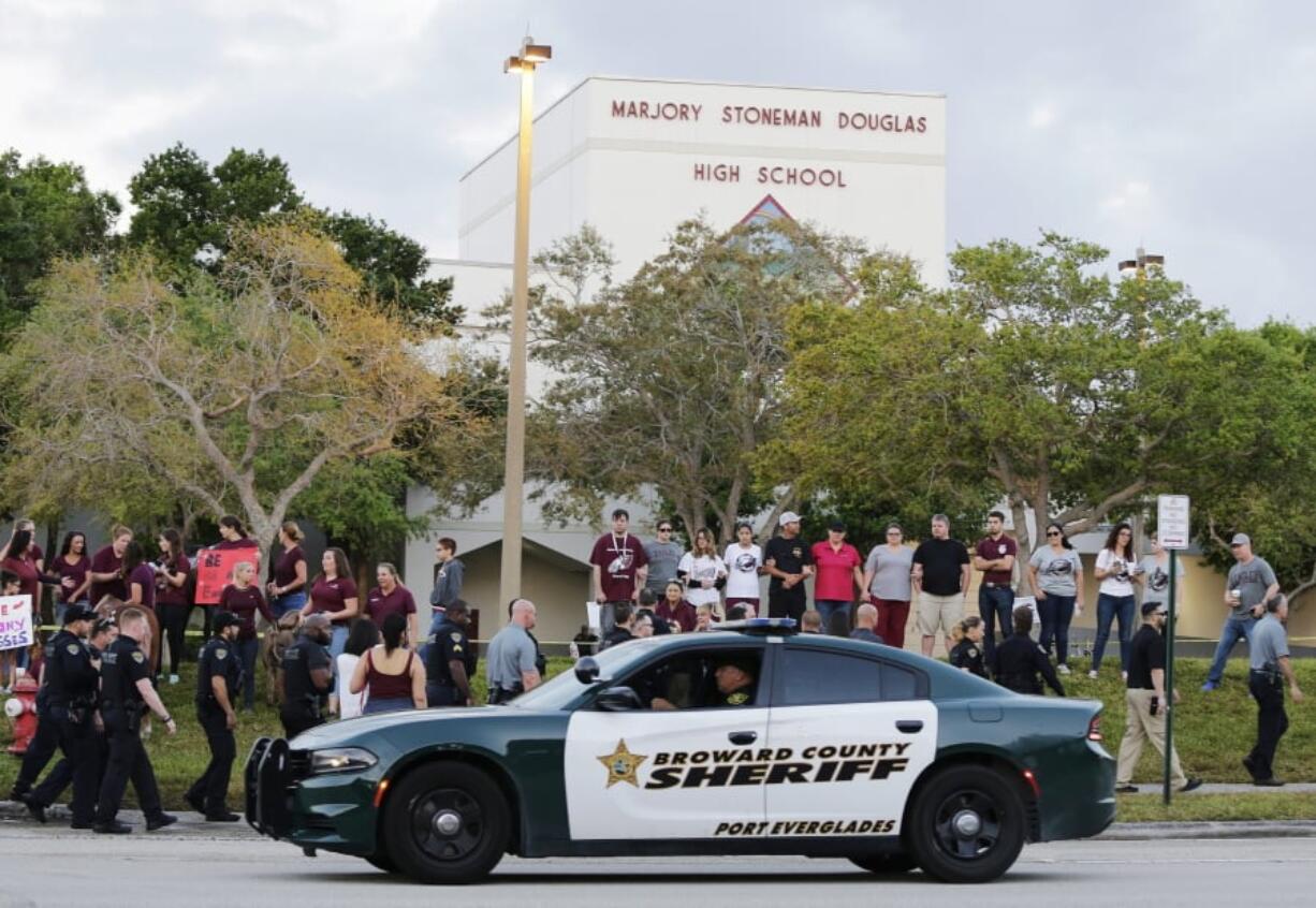 FILE - In this Feb. 28, 2018 file photo, a police car drives near Marjory Stoneman Douglas High School in Parkland, Fla., as students return to class for the first time since a former student opened fire there with an assault weapon. Survivors and family members of the slain victims of the school shooting in Parkland had plans Wednesday, April 10, 2019, to sue the school district, the sheriff’s office, a deputy and a school monitor, claiming their negligence allowed the massacre to happen.