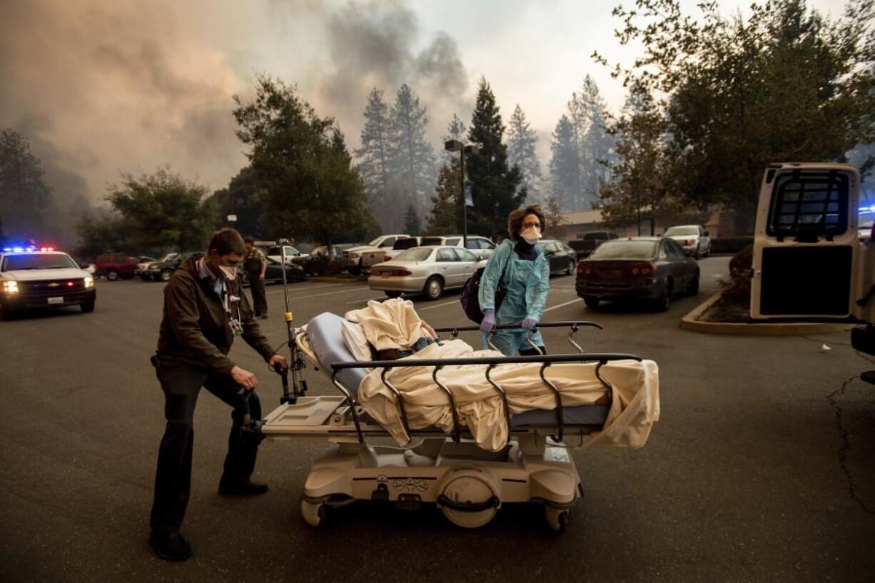 FILE - This Nov. 8, 2018, file photo shows Medical personnel evacuate patients as the Feather River Hospital burns while the Camp Fire rages through Paradise, Calif. Tens of thousands of people fled the fast-moving wildfire.