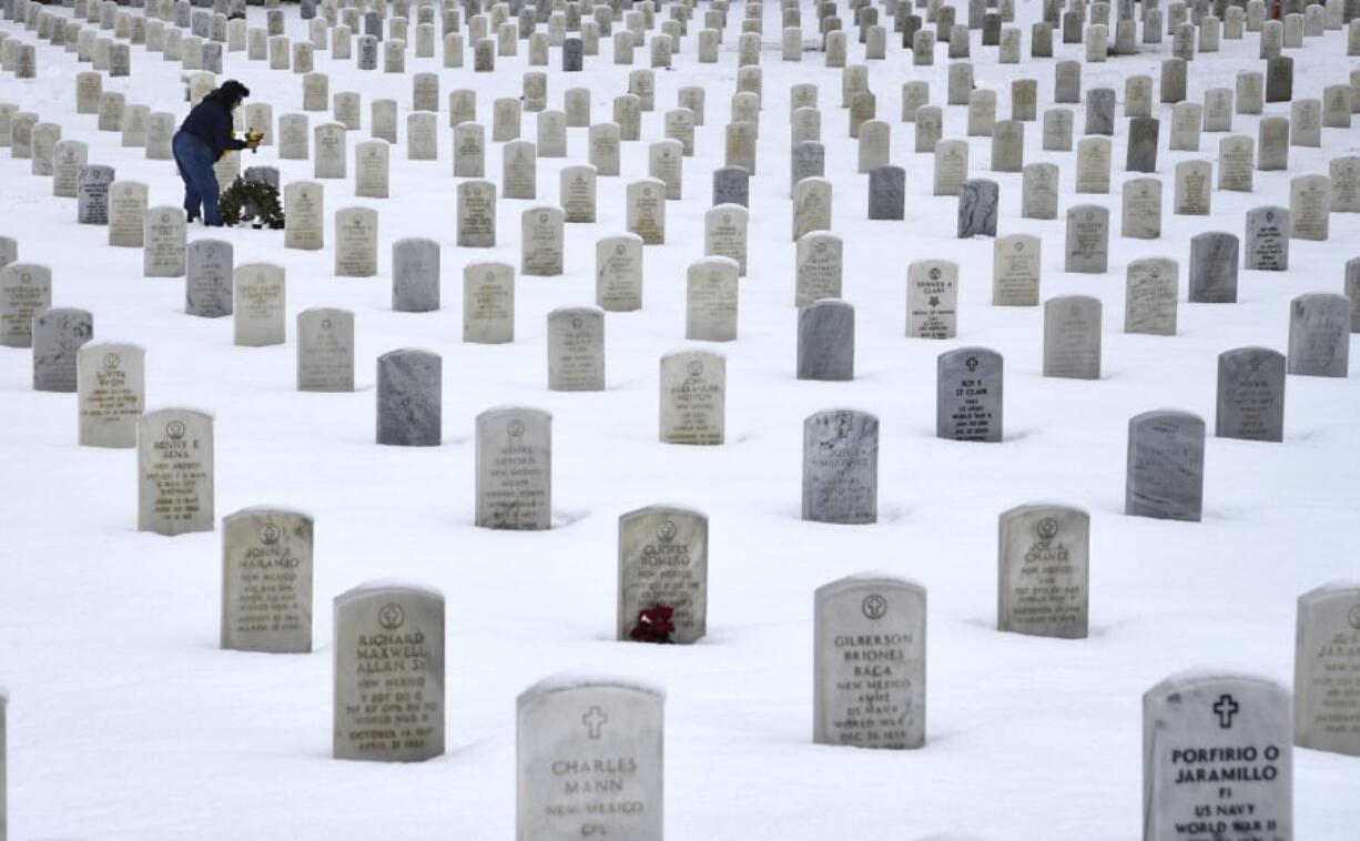 A woman places flowers on the grave of a loved one Jan. 11 at the Santa Fe National Cemetery in Santa Fe, N.M., which is administered by the United States Department of Veterans Affairs.