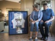 Beth and John Moritz sit next to a framed jersey and photo from the college sports career of their son, Zach Moritz. Zach died by suicide in 2015 after more than two years of struggling with the symptoms of Lyme disease. At top from left, Zach at a Super Bowl party a few months before he died; in the outdoors where he felt at home; and in a state high school basketball tournament game at the Tacoma Dome in 2005. He played for Columbia River High School.