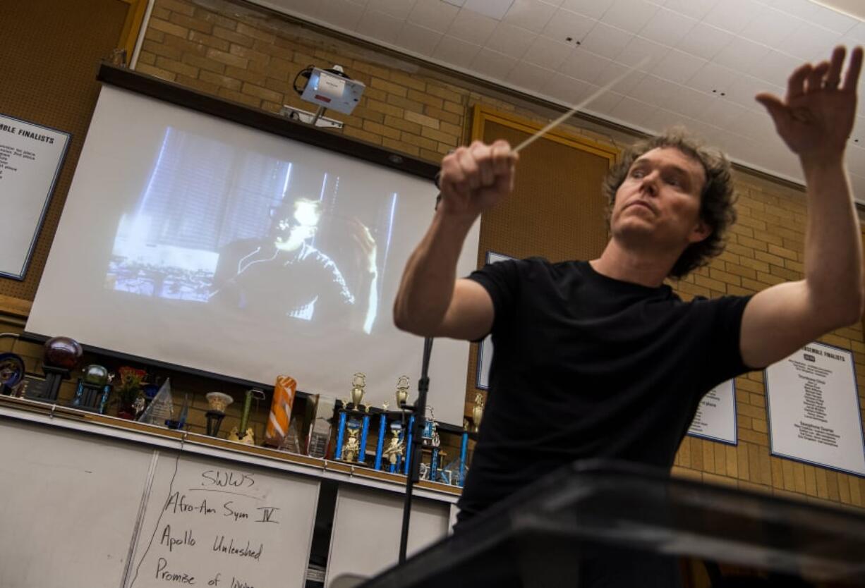 Rehearsal conductor Sam Ormson conducts the Southwest Washington Wind Symphony at Mountain View High School, while performance conductor Gerard Morris, on the screen above, listens in and critiques from Tacoma, where he’s on the faculty of the University of Puget Sound School of Music.