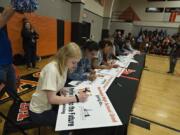 Shelby Jolly, 18, a Washougal High School senior, foreground, signs her name on a poster as she joins fellow classmates in celebrating their post-high school plans. Jolly, who was part of the group heading to Clark College in the fall, took part in Washougal’s first College and Career Signing Day. Students signed lawn signs to announce what college, branch of the military or apprenticeship program they plan to attend after graduating.