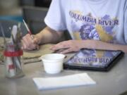 Cadence Oneil, 15, references her iPad while working on a pottery project at Columbia River High School on Thursday morning. Vancouver Public Schools is switching to Chromebooks in high schools next year after four years of using iPads.