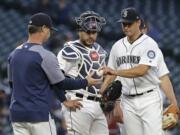 Seattle Mariners starting pitcher Marco Gonzales, right, hands the ball to manager Scott Servais, left, as catcher Omar Narvaez, center, looks on during the fifth inning of a baseball game against the Texas Rangers, Tuesday, May 28, 2019, in Seattle. (AP Photo/Ted S.