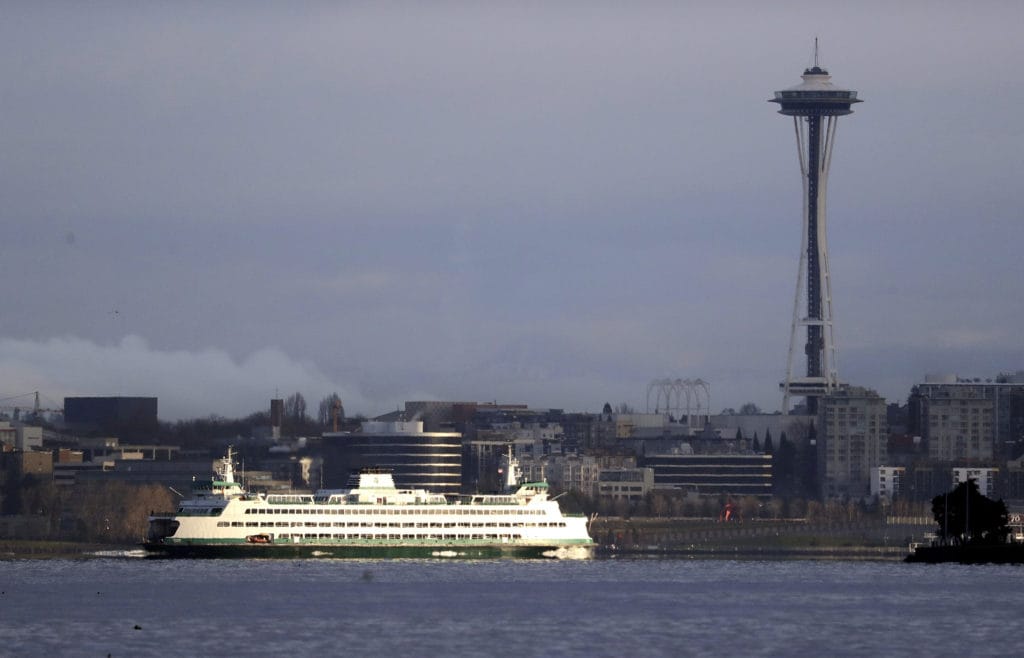 A Washington State ferry heading into Elliott Bay is illuminated by the sun as the city behind remains under clouds in Seattle in 2018.