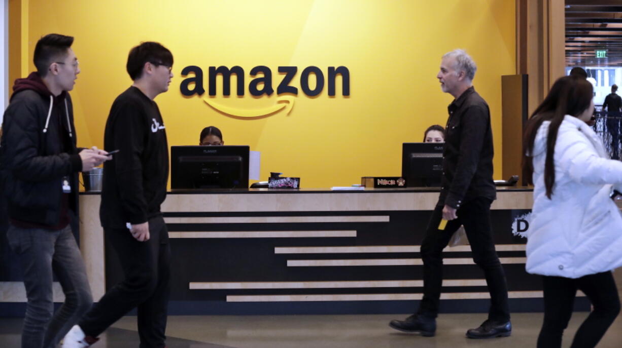 FILE - In this Nov. 13, 2018 file photo, employees walk through a lobby at Amazon’s headquarters in Seattle. On Friday, May 3, 2019, shares in Amazon are moving higher after billionaire investor Warren Buffett said his firm has been buying the online retailer.